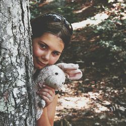 Girl holding bunny toy while hiding behind tree trunk