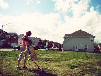 Full length of girl playing with dog on field against cloudy sky