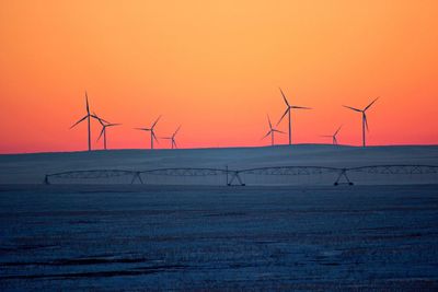 Wind turbines on land against sky during sunset