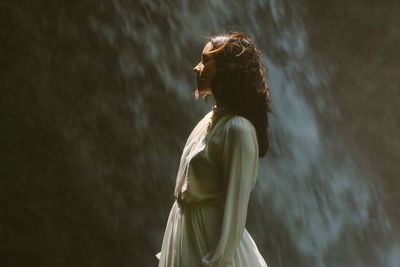 Side view of woman standing against waterfall