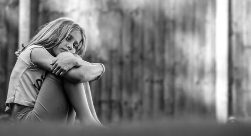 Portrait of thoughtful girl hugging knees while sitting against wall