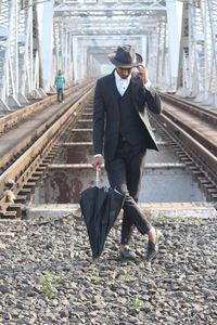 Full length of man holding umbrella at railroad station