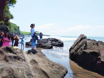 People on rocks by sea against sky