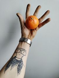 Cropped hand of man holding orange against white background