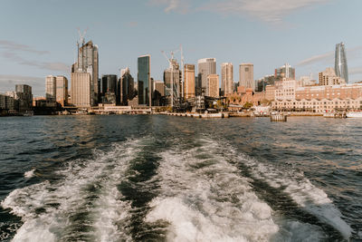 Sea by modern buildings against sky in city