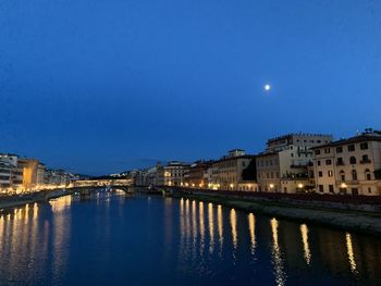 Illuminated buildings by river against sky at night