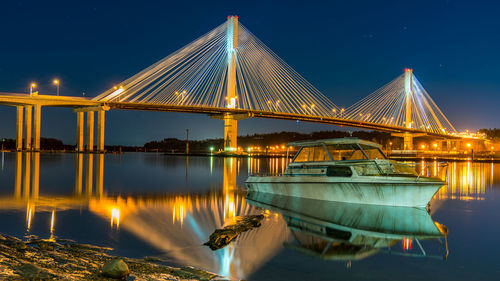 Illuminated suspension bridge over river against sky at night