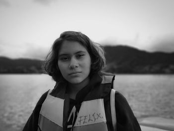 Portrait of teenage girl standing by lake against sky