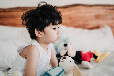 Cute boy sitting with toys on bed at home