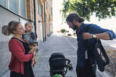 Mother with son looking at man wearing baby carrier on sidewalk