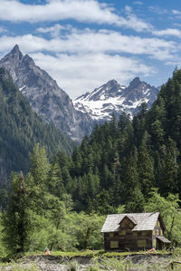 Log cabin against trees and mountains against cloudy sky