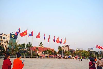 People by flags in city against clear sky