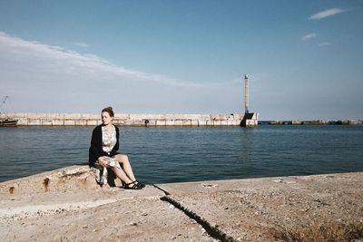 Full length of woman sitting at promenade against sky