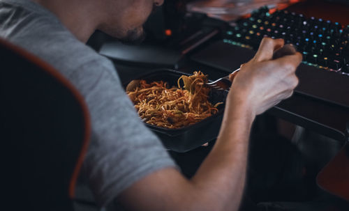 Young caucasian guy gamer eating wok food delivered in a black container with a fork