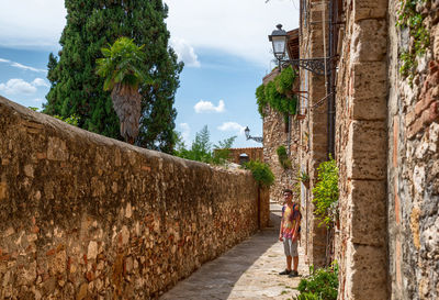 Woman walking in alley amidst buildings against sky