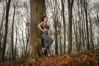 Sporty woman wearing activewear resting against a tree after exercise or running. 