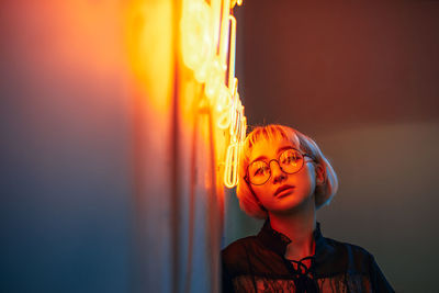 Close-up portrait of woman by illuminated wall