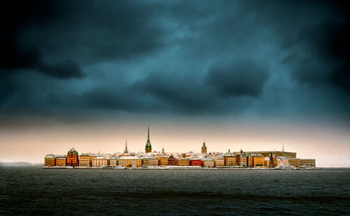 View of city at waterfront against dramatic sky