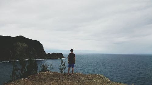 Rear view of man standing at beach against sky