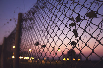 Close-up of chainlink fence against sky during sunset