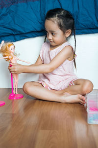 Cute girl playing with doll while sitting on floor