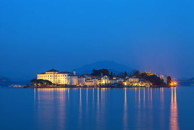 Illuminated buildings by sea against sky at dusk