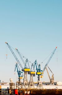 Cranes at commercial dock against clear sky