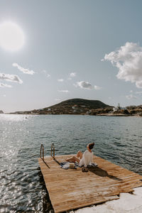 Rear view of woman sitting on pier by sea