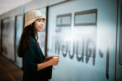 Young woman looking away while standing against wall