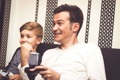 Cheerful father and son playing video games while sitting on sofa