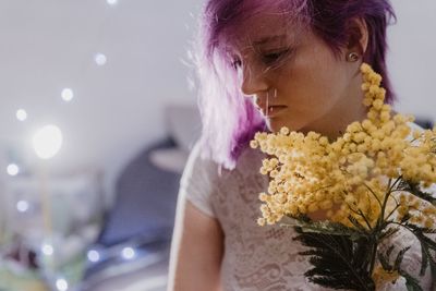 Young woman holding flowering plant standing at home