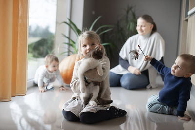 Mother with her three children playing with a cat on the floor at home