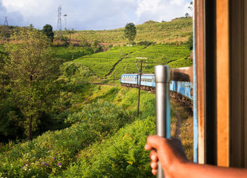 Cropped hand of person holding handle of train against landscape and sky