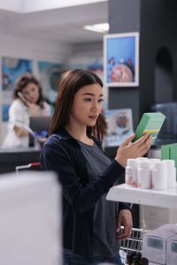 Portrait of young woman using mobile phone while standing in office