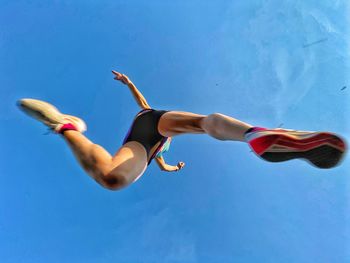 Low angle view of man jumping against blue sky