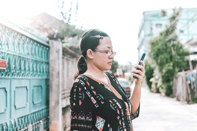 Side view of woman using phone while standing on road