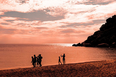 People on beach against sky during sunset