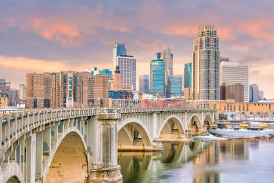 Arch bridge over river by buildings against sky during sunset