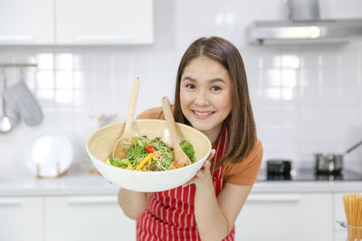 Portrait of smiling young woman holding ice cream at home