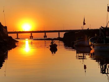 Silhouette boats moored in water against orange sky