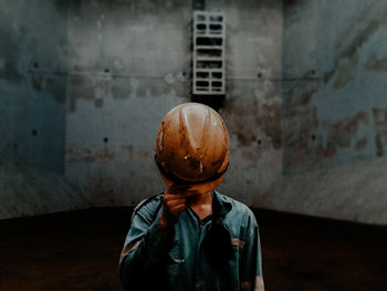 Worker covering face by hardhat while standing against wall