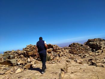 Rear view of man on rock against blue sky