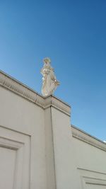 Low angle view of bird perching on building against clear blue sky