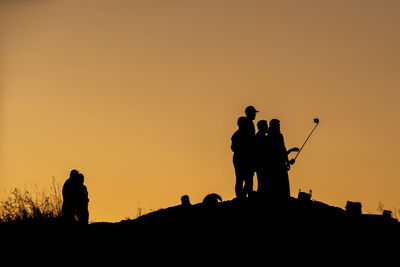Silhouette people standing on land against clear sky during sunset