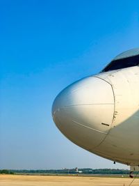 View of airplane on airport runway against clear blue sky