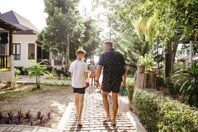 Rear view of father walking with son on footpath by bungalows during vacation