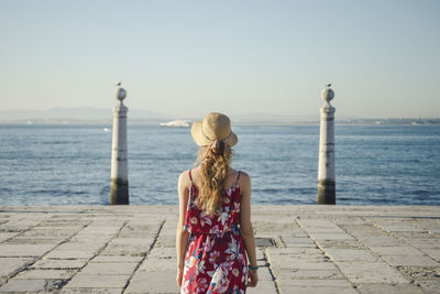 Rear view of woman standing by sea against sky