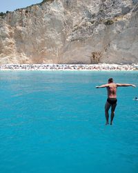 Rear view of shirtless man standing on rock in sea