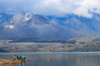 People sitting by lake against mountain range