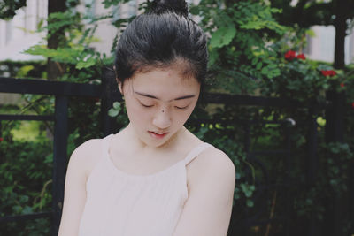 Young woman looking away while standing against trees